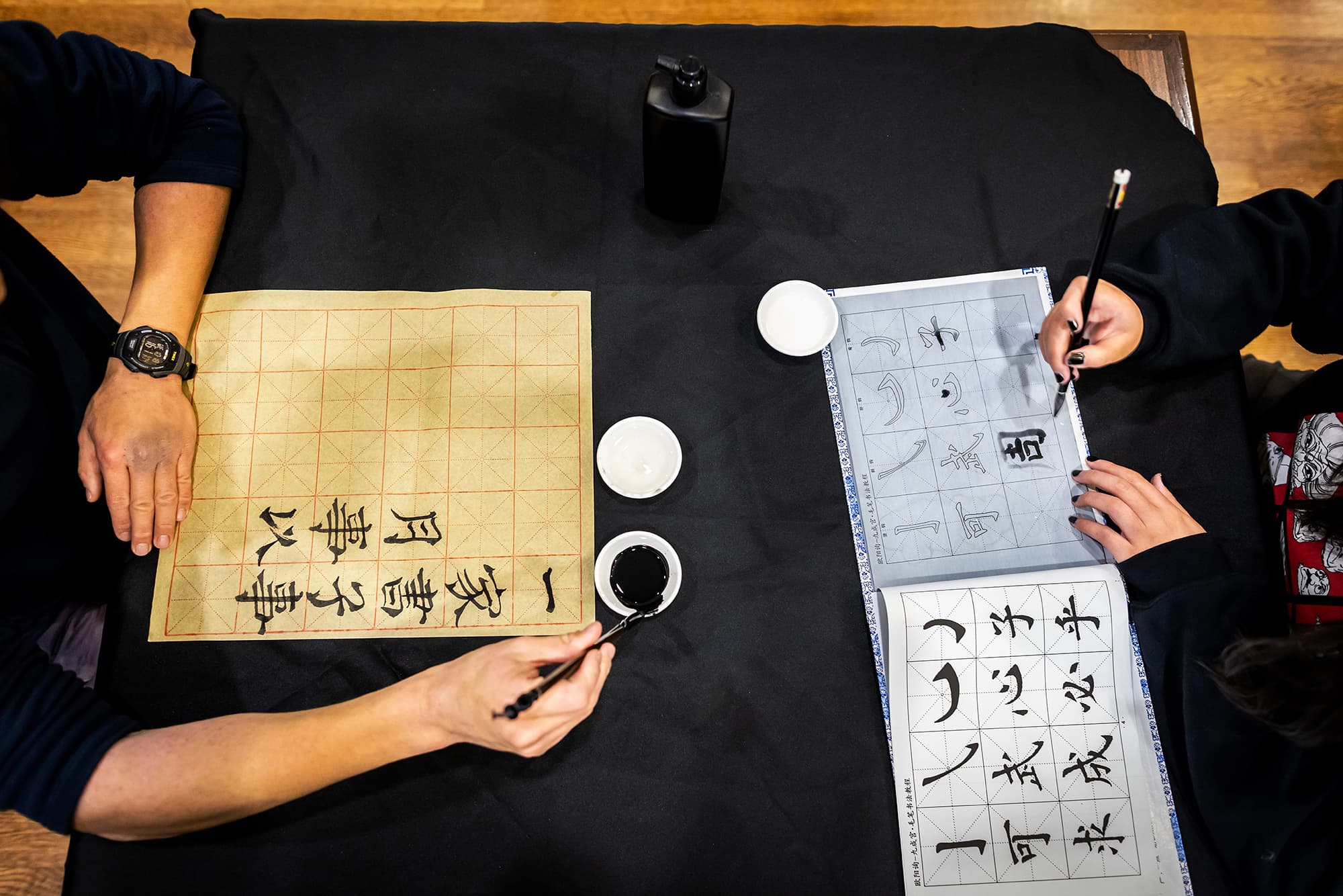 Two people practicing chinese calligraphy